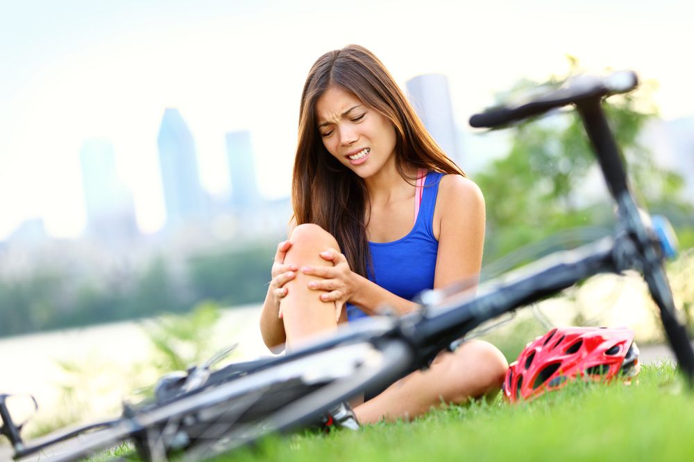 Woman holding knee in pain next to bicycle in park